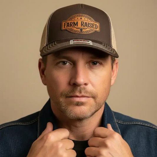 A man wearing a brown and beige trucker hat with a 'Farm Rated' patch, paired with a dark denim jacket, set against a plain beige background.